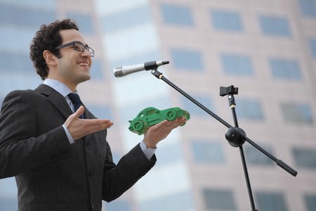 Businessman holding a green car model while giving speechの写真素材