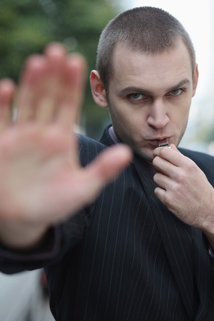 Businessman showing stop gesture while blowing whistleの写真素材