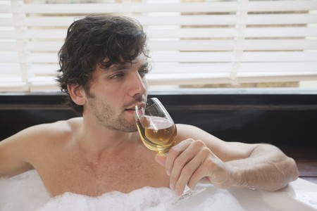 Man enjoying champagne while relaxing in bubble bathの写真素材