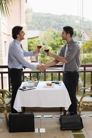 Businessmen shaking hands and toasting red wine