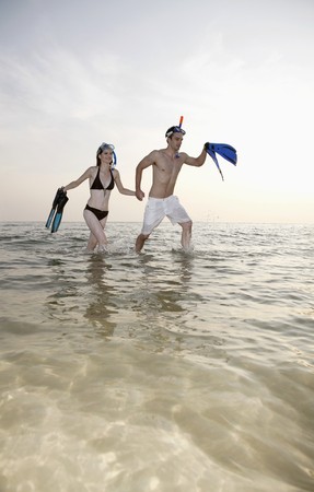 Man and woman running on beach with snorkeling gearの写真素材
