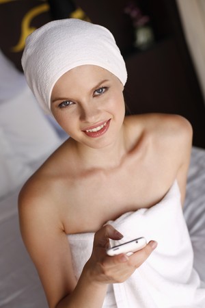 Woman with towel wrapped around head text messaging on phoneの写真素材