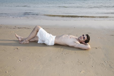 Man with bare chest lying down with hands behind head on beachの写真素材