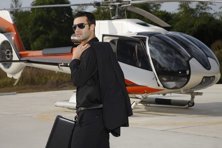 Businessman with briefcase standing at helipad, helicopter in the backgroundの写真素材