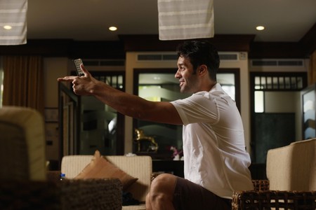 Man cheering while watching television with remote control in handの写真素材