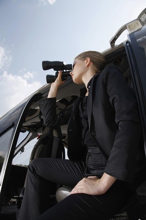 Businesswoman looking through binoculars from helicopterの写真素材