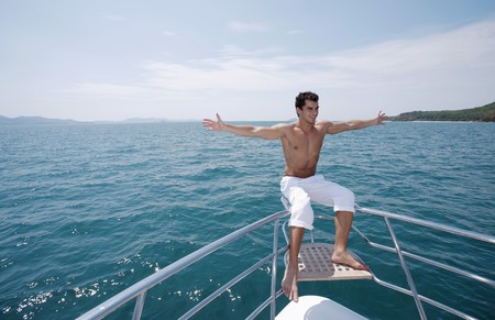 Man with arms outstretched sitting on yacht's railingの写真素材