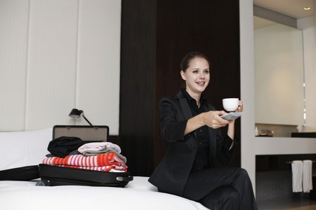 Businesswoman enjoying a cup of coffee with remote control in handの写真素材