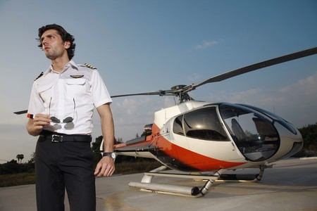 Pilot holding sunglasses with helicopter in the backgroundの写真素材