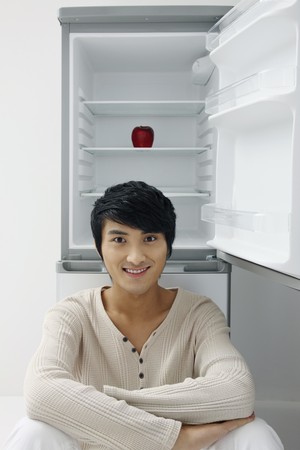 Man sitting in front of refrigerator, red apple inside refrigeratorの写真素材