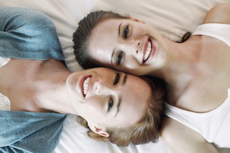Women lying on bed with heads side by sideの写真素材