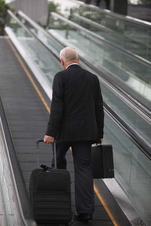 Businessman on escalator, pulling suitcaseの写真素材