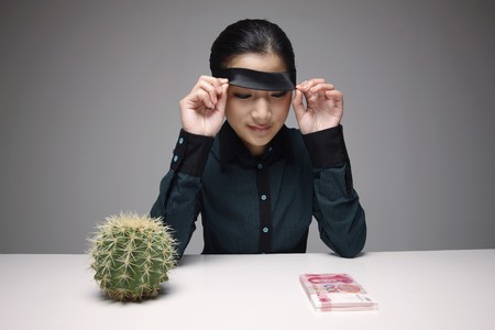 Woman lifting up blindfold, looking at stack of paper currencyの写真素材
