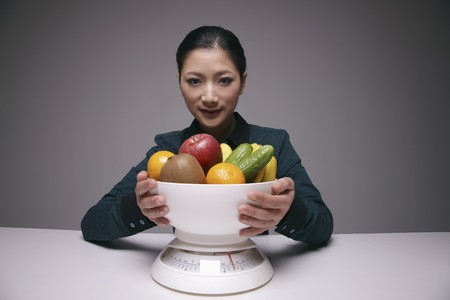 Woman holding a bowl of fruits and vegetable on scaleの写真素材