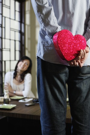 Young couple, man hiding present behind backの写真素材