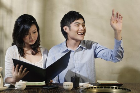 Man gesturing to order food, woman reading menuの写真素材