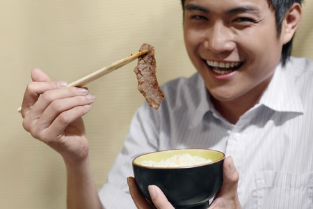 Man holding a bowl of rice and a piece of grilled meatの写真素材