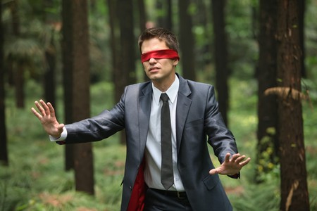 Businessman with blindfold walking aimlessly in the forestの写真素材