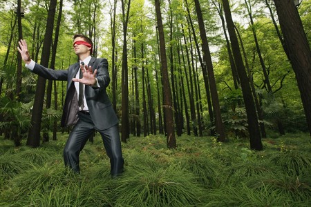 Businessman with blindfold walking aimlessly in the forestの写真素材