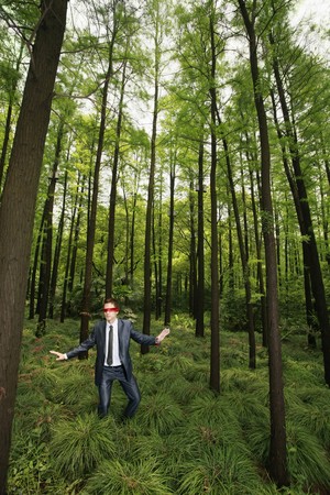 Businessman with blindfold walking aimlessly in the forestの写真素材