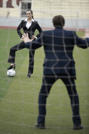 Businesswoman standing on football with businessman as the goal keeperの写真素材