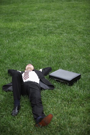 Businessman lying down on green grassの写真素材
