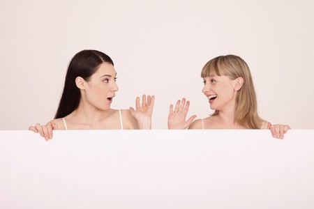 Women standing behind blank placard greeting each otherの写真素材