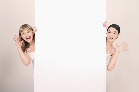 Women peeking out from behind blank placard with hand gesturesの写真素材