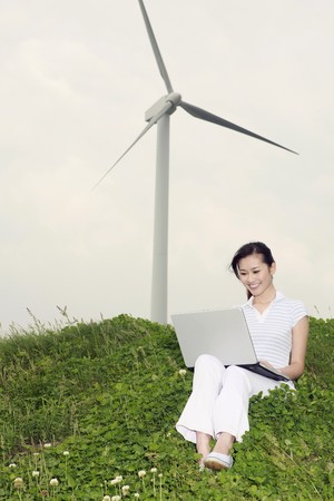 Women using laptop outdoors with wind mill in the backgroundの写真素材