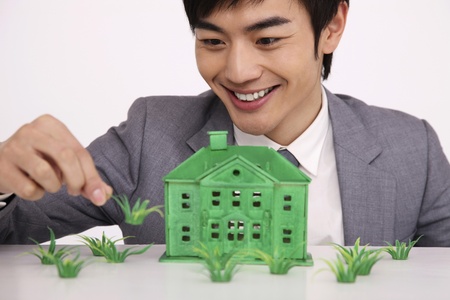 Man holding grass with green house model on the tableの写真素材
