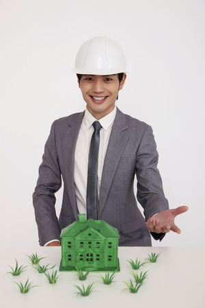 Man wearing safety helmet showing green house model with grass on tableの写真素材