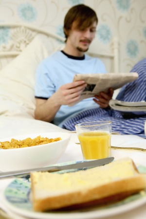 Breakfast in bed, with man reading newspaper in the backgroundの写真素材