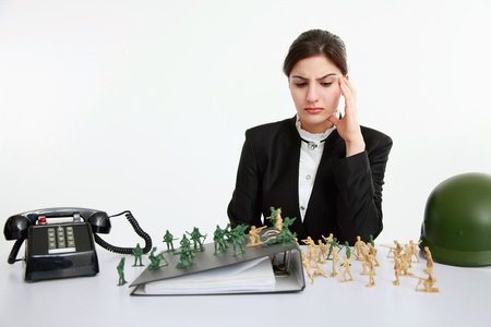 Businesswoman frowning while looking at all the toy soldiers on the tableの写真素材