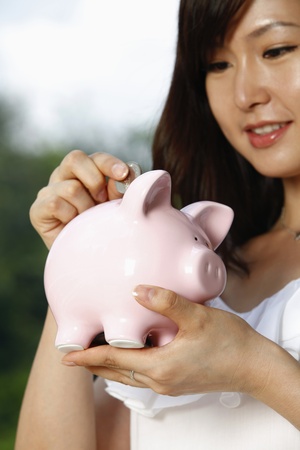 Woman putting coin into piggy bankの写真素材