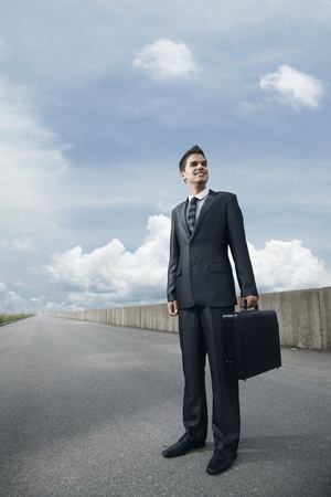 Businessman with bag standing on an empty roadの写真素材