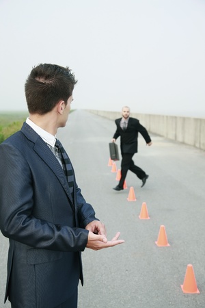 Businessman running in between traffic cones, another businessman watchingの写真素材