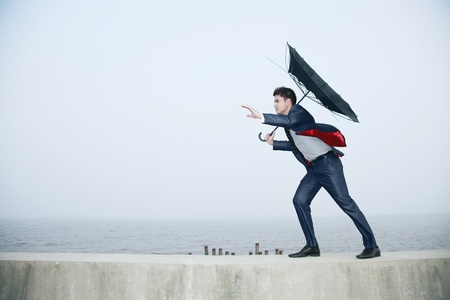 Businessman with an umbrella, wind blowing his umbrella awayの写真素材