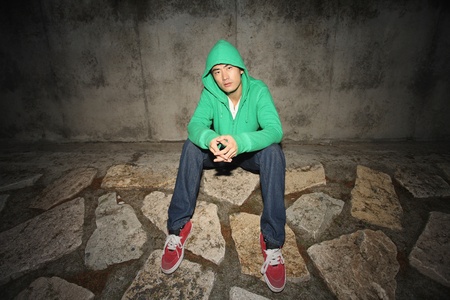 Man in hooded shirt sitting on the ground outdoors