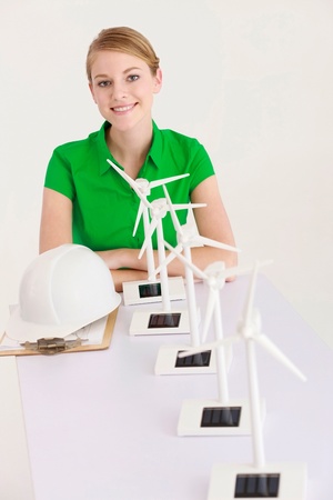 Businesswoman sitting with a row of wind turbine models on the tableの写真素材