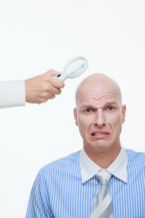 Hand holding a magnifying glass near a bald man's head
