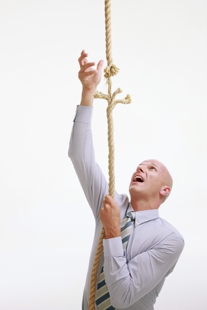 Businessman climbing up a fraying ropeの写真素材