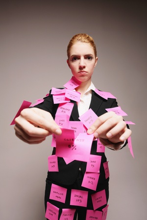 Businesswoman covered with adhesive notes tearing up messages on paperの写真素材