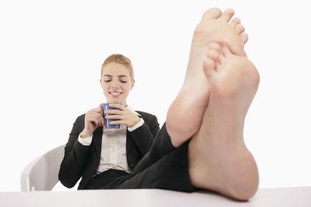 Businesswoman resting with her legs up on a table while drinking coffeeの写真素材