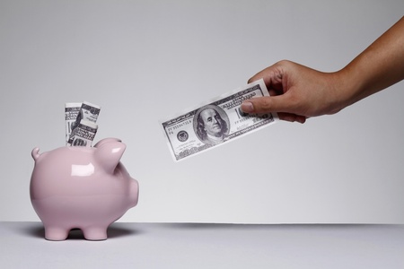 Hand holding US dollar, US dollar in piggy bank slotの写真素材