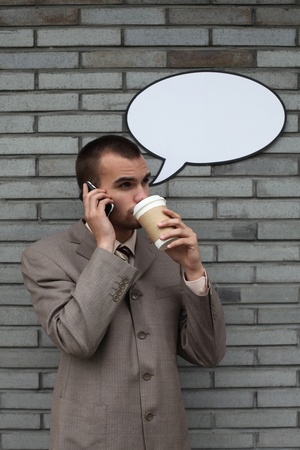 Businessman with speech bubble talking on the phone and drinking coffeeの写真素材