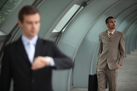 Businessman holding briefcase while another businessman is looking at his watchの写真素材