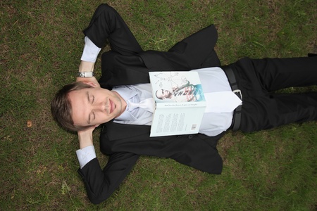 Businessman lying on the grass with book on his chestの写真素材