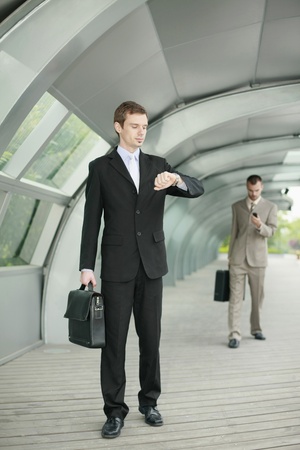 Businessman looking at his watch while another businessman is in the backgroundの写真素材