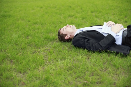Businessman lying on the grass with book on his bodyの写真素材