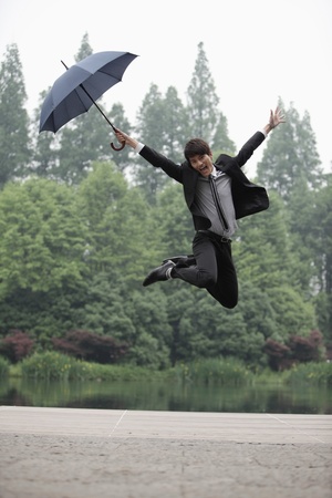 Businessman with an umbrella jumping in the airの写真素材